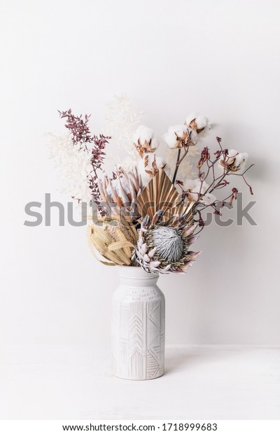 Beautiful dried flower\
arrangement in a stylish ceramic white vase. Dried flowers include\
pink proteas, banksia, gold palm leaf, kangaroo paw, cotton and\
ruscus leaves.