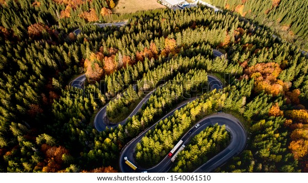 Beautiful drone view of winding forest road in the\
middle of mountains. Colourful landscape with rural road, trees\
with yellow leaves. 