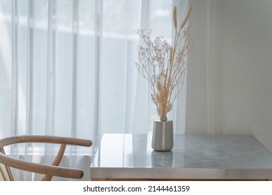 Beautiful dry flowers in an aluminum metal vase with light shines through the translucent curtains of the windows for decoration home interior on a wooden table. Concept modern building contemporary. - Shutterstock ID 2144461359