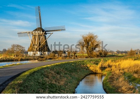 Beautiful dutch landscape, curvy road along the traditional windmill and old willow tree on a sunny day