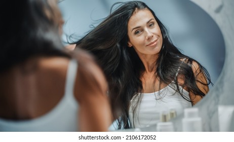 Beautiful Early Middle Aged Woman Looks into Bathroom Mirror Touches Her Lush Black Hair, Admires Her Looks. Concept for Happiness, Wellbeing, Natural Beauty, Organic Skin Care Products - Shutterstock ID 2106172052