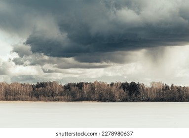 Beautiful early spring landscape with frozen lake, forest on the horizon and dramatic sky with grey clouds and snowfall in the distance, storm coming - Powered by Shutterstock