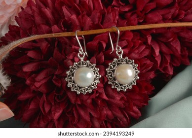 Beautiful earrings with pearls and filigree decoration with artificial flowers background - Shutterstock ID 2394193249