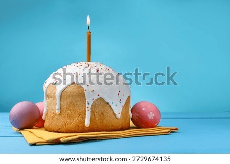 Beautiful Easter cake with burning candle and eggs on blue wooden table. Space for text