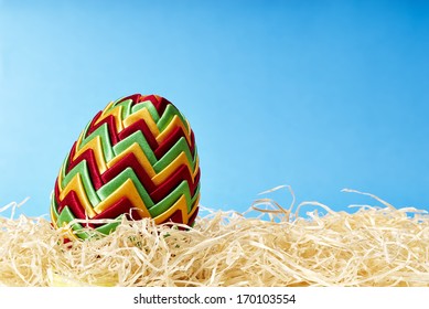 Beautiful easter egg in hay on blue background. Copy space.