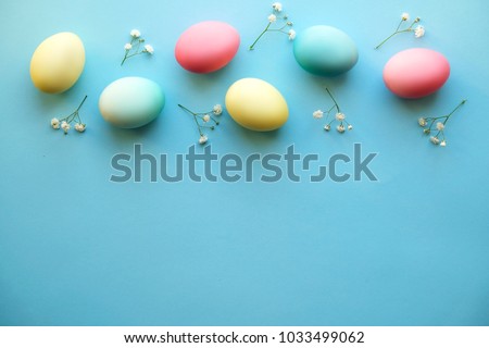 Beautiful easter table setting composition. A row of pastel color eggs, pink, blue and yellow, white gypsophila wildflower flower on blue background. Happy Easter greeting card. Top view, copy space.