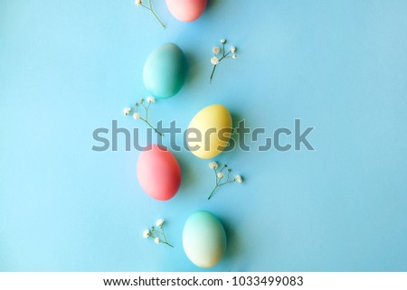 Beautiful easter table setting composition. A row of pastel color eggs, pink, blue and yellow, white gypsophila wildflower flower on blue background. Happy Easter greeting card. Top view, copy space.