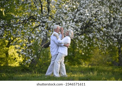 Beautiful elderly couple dancing in the apple orchard. High quality photo