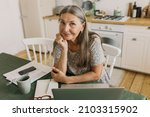 Beautiful elderly female author posing in home office. Creative workplace with paper, laptop, cup of coffee. Work from home, fertile imagination, inspiration, journalist concept