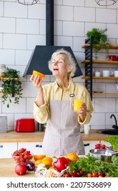 Beautiful Elderly Gray Haired Senior Woman Cook In Cozy Kitchen With Fresh Organic Vegetables, Making  Fresh Orange Juice On Table And Cooking Healthy Vegetable Salad, Healthy Food Active Life