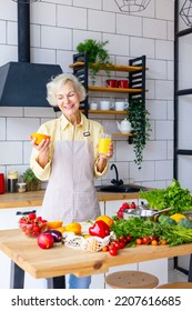 Beautiful Elderly Gray Haired Senior Woman Cook In Cozy Kitchen With Fresh Organic Vegetables, Making  Fresh Orange Juice On Table And Cooking Healthy Vegetable Salad, Healthy Food Active Life