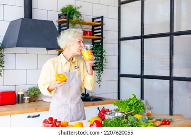 Beautiful Elderly Gray Haired Senior Woman Cook In Cozy Kitchen With Fresh Organic Vegetables, Making  Fresh Orange Juice On Table And Cooking Healthy Vegetable Salad, Healthy Food Active Life