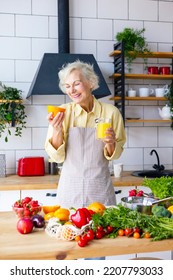 Beautiful Elderly Gray Haired Senior Woman Cook In Cozy Kitchen With Fresh Organic Vegetables, Making  Fresh Orange Juice On Table And Cooking Healthy Vegetable Salad, Healthy Food Active Life