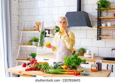 Beautiful Elderly Gray Haired Senior Woman Cook In Cozy Kitchen With Fresh Organic Vegetables, Making  Fresh Orange Juice On Table And Cooking Healthy Vegetable Salad, Healthy Food Active Life