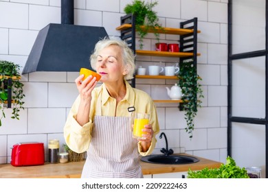 Beautiful Elderly Gray Haired Senior Woman Cook In Cozy Kitchen With Fresh Organic Vegetables, Making  Fresh Orange Juice On Table And Cooking Healthy Vegetable Salad, Healthy Food Active Life