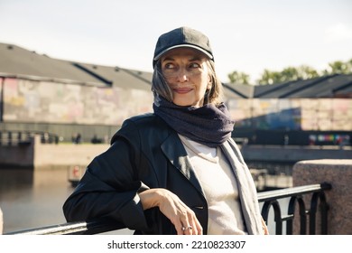 Beautiful Elderly Woman In  Cap And  Black Raincoat By  Embankment