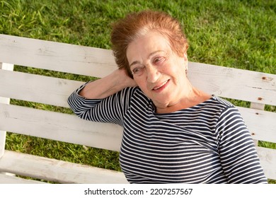 Beautiful Elderly Woman, Pensioner Outside. Portrait Of A Positive Granny On Bench In The Park. Sunny Day. Concept Of Old Age, Good Mood, Health Insurance. Life Style. Outdoor. Retired Senior Lady 80+