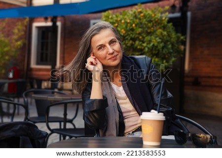 Beautiful elderly woman at  table in  street cafe on  warm autumn day