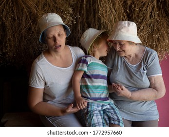 Beautiful Elderly Woman With Wrinkles, Young Girl And Boy From Same Family. Three Different Ages Of Similar People. Mother, Adult Daughter And Grandson In Identical Hats On Background Of Dry Flowers