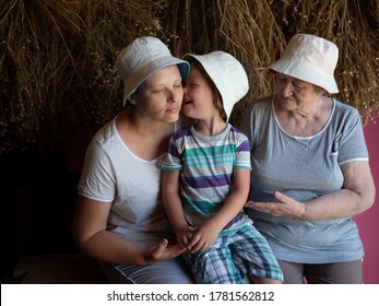 Beautiful Elderly Woman With Wrinkles, Young Girl And Boy From Same Family. Three Different Ages Of Similar People. Mother, Adult Daughter And Grandson In Identical Hats On Background Of Dry Flowers