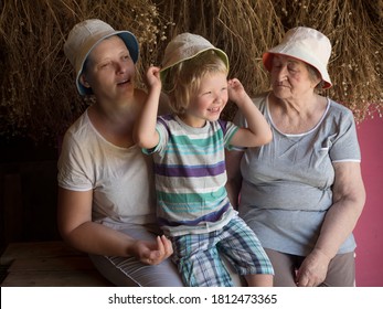 Beautiful Elderly Woman With Wrinkles, Young Girl And Boy From Same Family. Three Different Ages Of Similar People. Mother, Adult Daughter And Grandson In Identical Hats On Background Of Dry Flowers