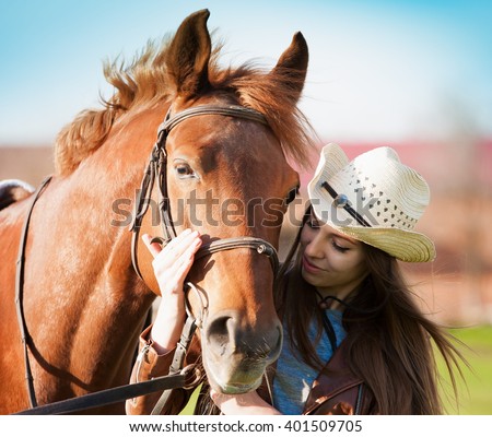 Beautiful elegance woman cowgirl nearby muzzle horse. Has smiling face, brown leather jacket and hat. Has slim body. Portrait nature. People and animals. Equestrian. Close up. American ranch riding