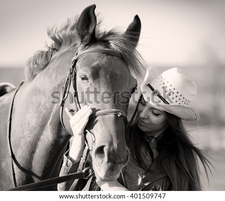 Beautiful elegance woman cowgirl nearby muzzle horse. Has smiling face, brown leather jacket and hat. Has slim body. Portrait nature. People and animals. Equestrian. Close up. Black and white. Retro 