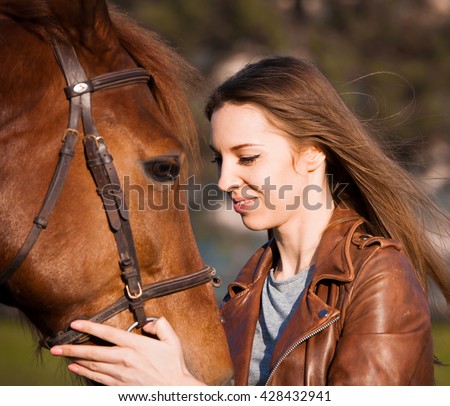 Beautiful elegance woman cowgirl nearby muzzle horse. Has smiling face, brown leather jacket and hat. Has slim body. Portrait nature. People and animals. Equestrian. Close up. American ranch.