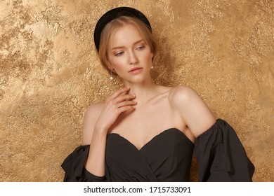 Beautiful Elegant Blonde Woman With Hairstyle Wearing Casual Clothes, Black Top And White Trousers With Band In Hair Standing Leaning On Golden Wall And Posing. Styish Fashion Female Model