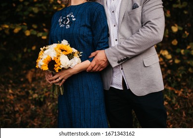 Beautiful Elegant Bride In Blue Wedding Dress With Long Sleeves, Hugged By Her Husband.. She Is Holding A Big Bouquet Of Flowers. Outdoors, On The Road. Close Up.