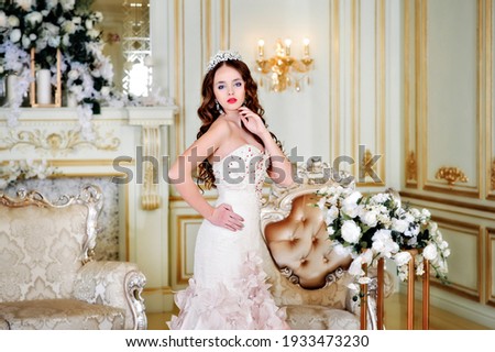 Beautiful elegant brunette young woman princess standing. Model in a golden interior, classic old rooms, French palace. Long dress.