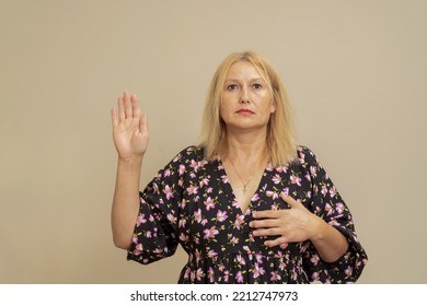 Beautiful Elegant Caucasian Woman On A Beige Isolated Background. Swearing With Hand On Chest And Fingers, Taking A Pledge Of Allegiance Oath.