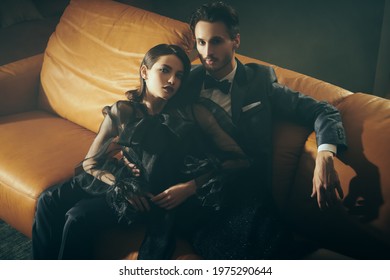 Beautiful Elegant Couple In Fashionable Evening Clothes Relaxing On A Leather Sofa In A Luxury Apartment. Glamorous Lifestyle. Fashion Shot.