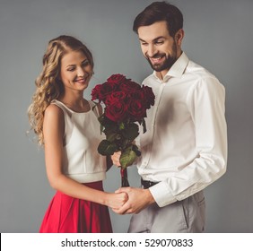 Beautiful elegant couple is holding hands and roses and smiling, on gray background - Shutterstock ID 529070833