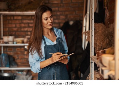 Beautiful elegant craft woman with long hair holding clipboard in hands in art modern studio - Powered by Shutterstock