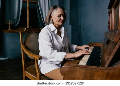 Beautiful elegant elderly woman sitting in front of the piano on a chair
