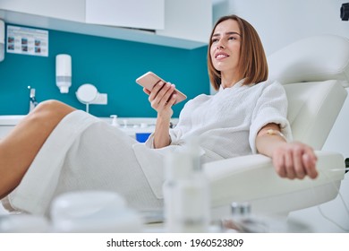 Beautiful elegant female sitting in armchair and getting intravenous vitamin drip treatment in beauty center