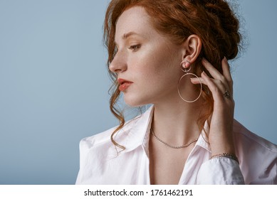 Beautiful elegant redhead freckled woman wearing luxury silver jewelry: earrings, chain, posing in studio, on blue background. Jewellery advertising conception. Close up profile portrait. Copy space