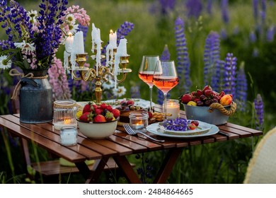 Beautiful elegant romantic dinner table decor, surprise day arrangement. Marriage proposal, engagement private party for two in a meadow. Sunset, golden hour. Cheese board, rose wine, fruits, lupine - Powered by Shutterstock