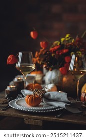 Beautiful elegant table setting for candlelight Thanksgiving Day dinner or Halloween party at home. Fancy dishware, porcelain plates. Floral centrepiece, pumpkins and burning candles as decor