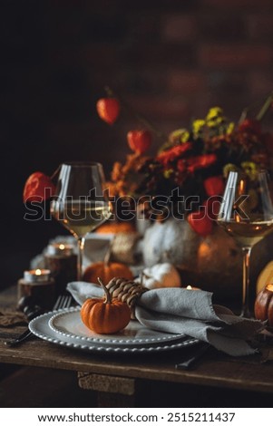 Beautiful elegant table setting for candlelight Thanksgiving Day dinner or Halloween party at home. Fancy dishware, porcelain plates. Floral centrepiece, pumpkins and burning candles as decor