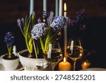 Beautiful elegant table setting for Easter celebration with fresh spring hyacinth flowers, burning candles. Romantic wedding dinner table decoration. Springtime, home gardening. Dark background