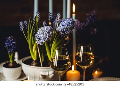 Beautiful elegant table setting for Easter celebration with fresh spring hyacinth flowers, burning candles. Romantic wedding dinner table decoration. Springtime, home gardening. Dark background