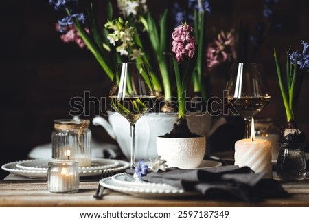 Beautiful elegant table setting for Easter celebration with fresh spring hyacinth flowers, burning candles. Romantic wedding dinner table decoration. Springtime, home gardening. Dark background