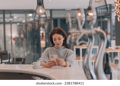 Beautiful and elegant woman sitting at the bar of a coffee shop looking at her cell phone, pensive and nostalgic. - Powered by Shutterstock