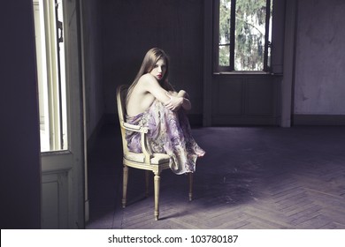 Beautiful elegant woman sitting on a chair in an empty room