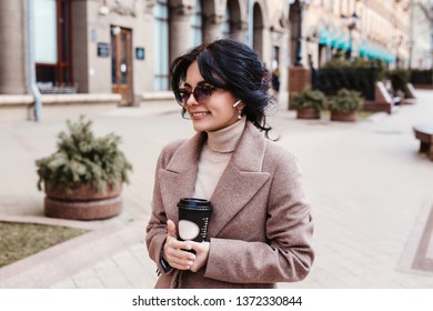 Beautiful Elegant Woman In Sunglasses And Coat With Airpods Outdoors