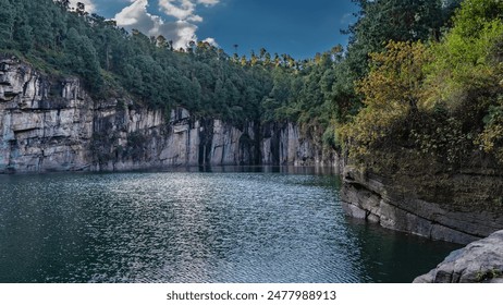 A beautiful emerald lake in the crater of an extinct volcano is surrounded by steep banks. Lush green vegetation on the rocks. Clouds in the blue sky. Madagascar. Tritriva Lake. - Powered by Shutterstock