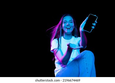 Beautiful emotional girl inviting for shopping, black friday, seasonal sales isolated over dark background in neon light. Cyber monday and online purchases. Art, fashion, emotions, ad - Powered by Shutterstock