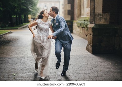 Beautiful emotional wedding couple smiling and kissing in rain in european city. Provence wedding. Stylish happy bride and groom running on background of old church in rainy street. - Powered by Shutterstock